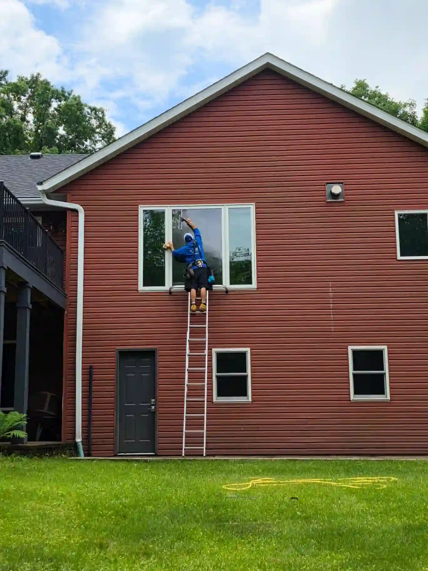 Starbrite technician cleaning a second-story window on a red-sided Twin Cities home