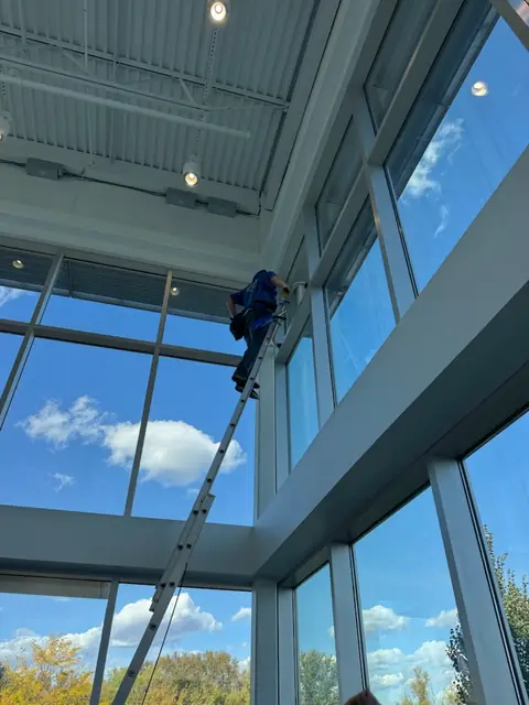 Window cleaner on an extension ladder cleaning upper clerestory windows in a commercial lobby in Brooklyn Park, Minnesota