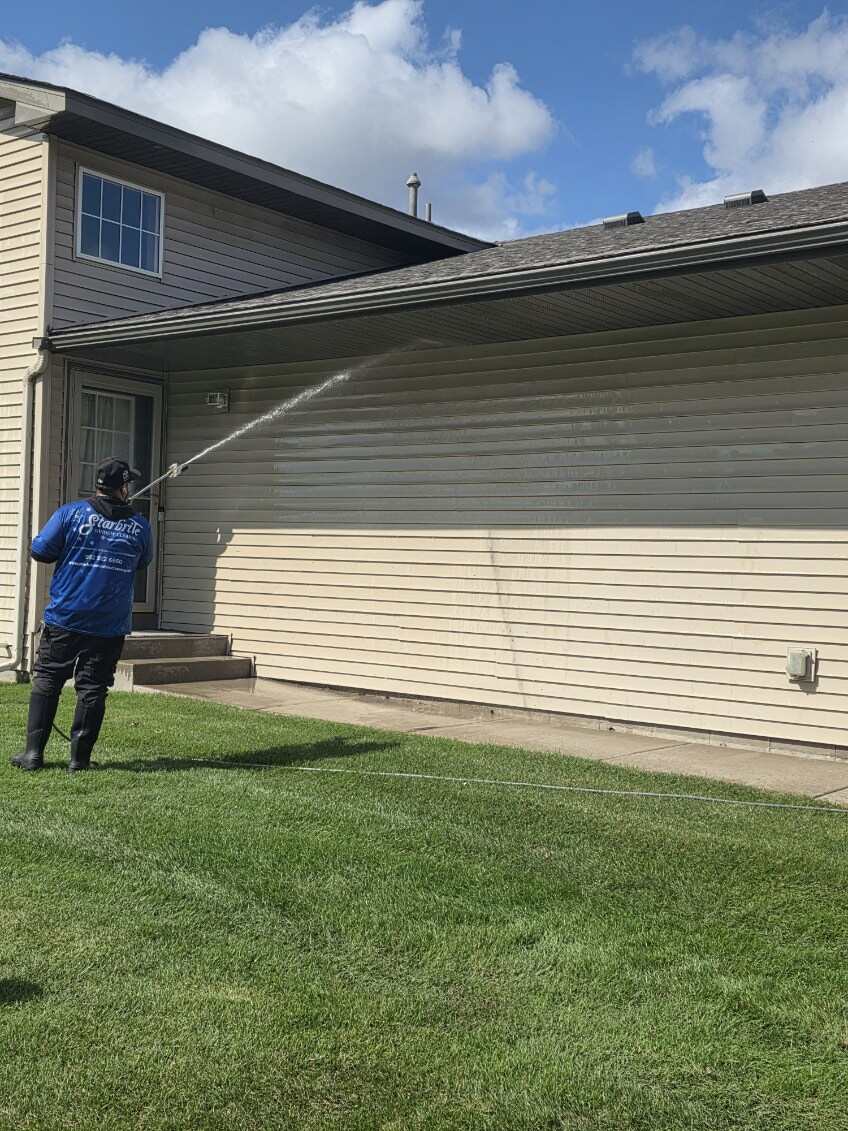 Starbrite technician soft-washing vinyl siding to remove dirt and algae