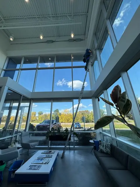 Starbrite technician on a tall ladder cleaning two-story lobby windows at a commercial building in Brooklyn Park, MN