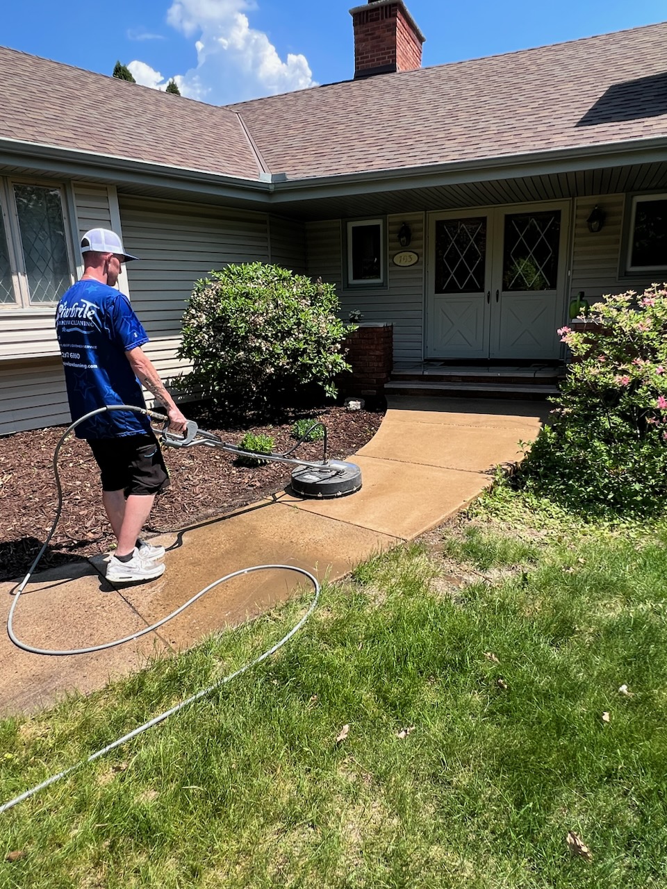 Starbrite technician using a surface cleaner to pressure wash a concrete walkway