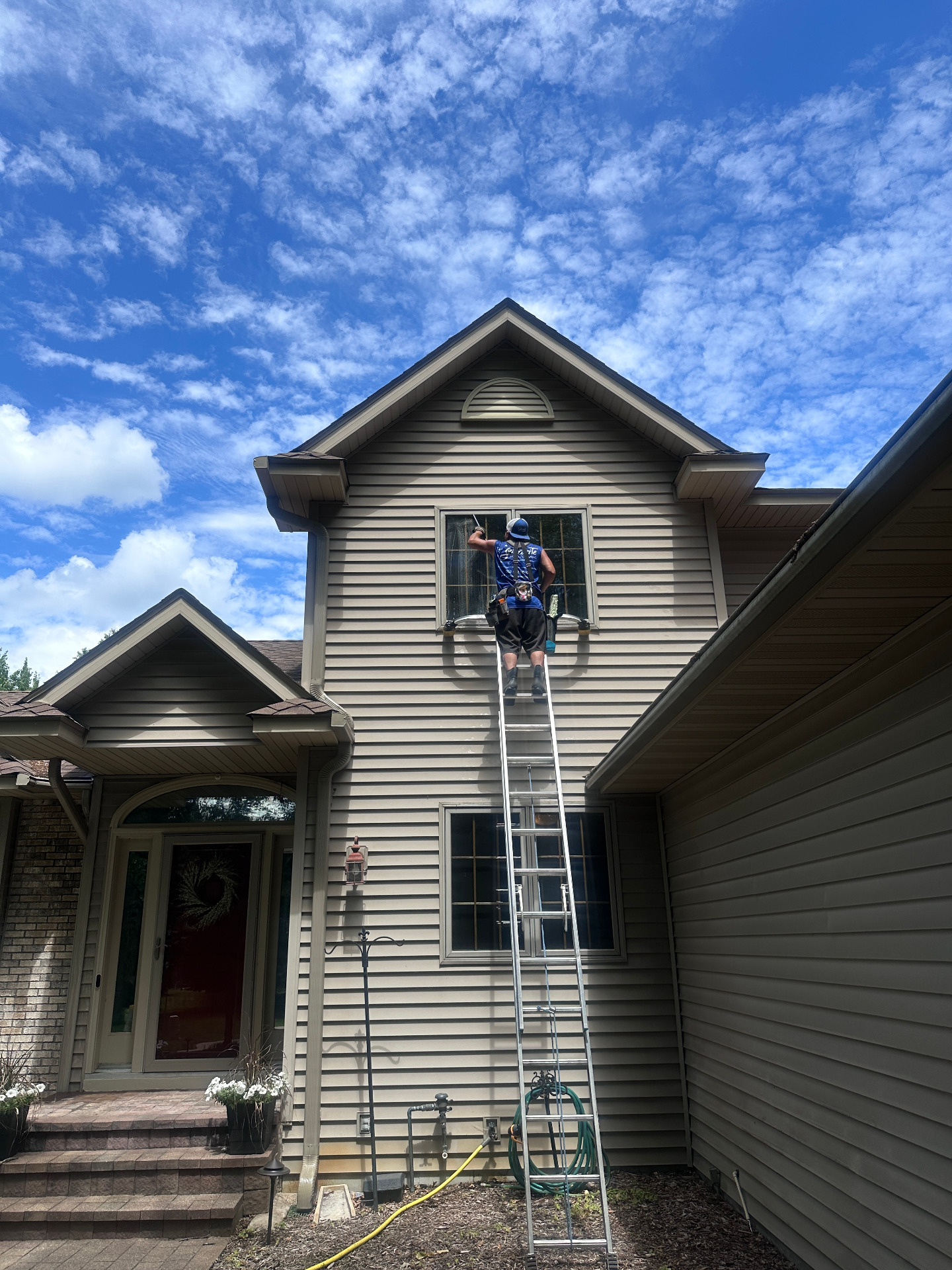 Starbrite technician cleaning second-story exterior windows from a ladder