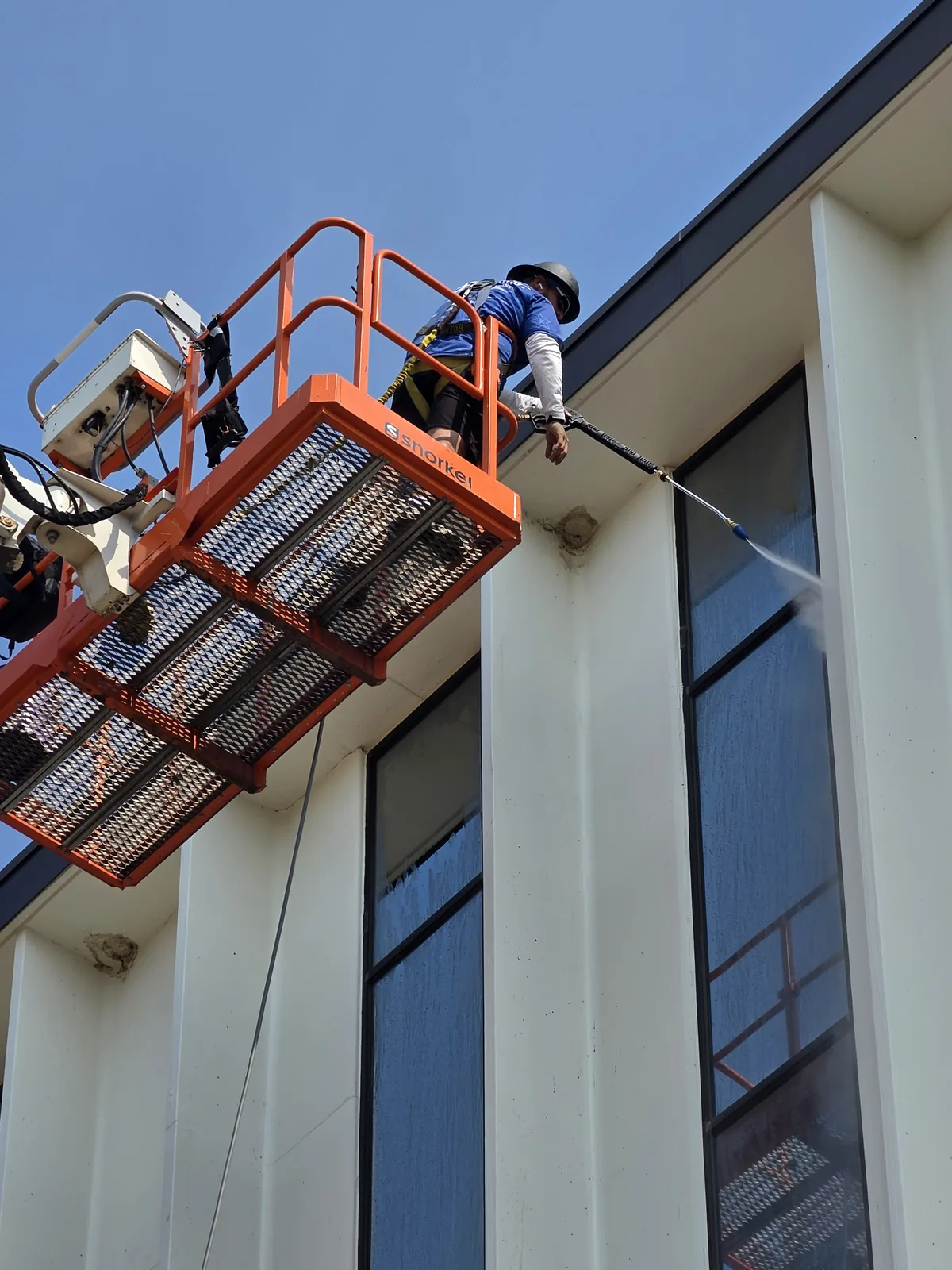 Starbrite Window Cleaning technician power washing the exterior of a Twin Cities commercial building from an aerial lift