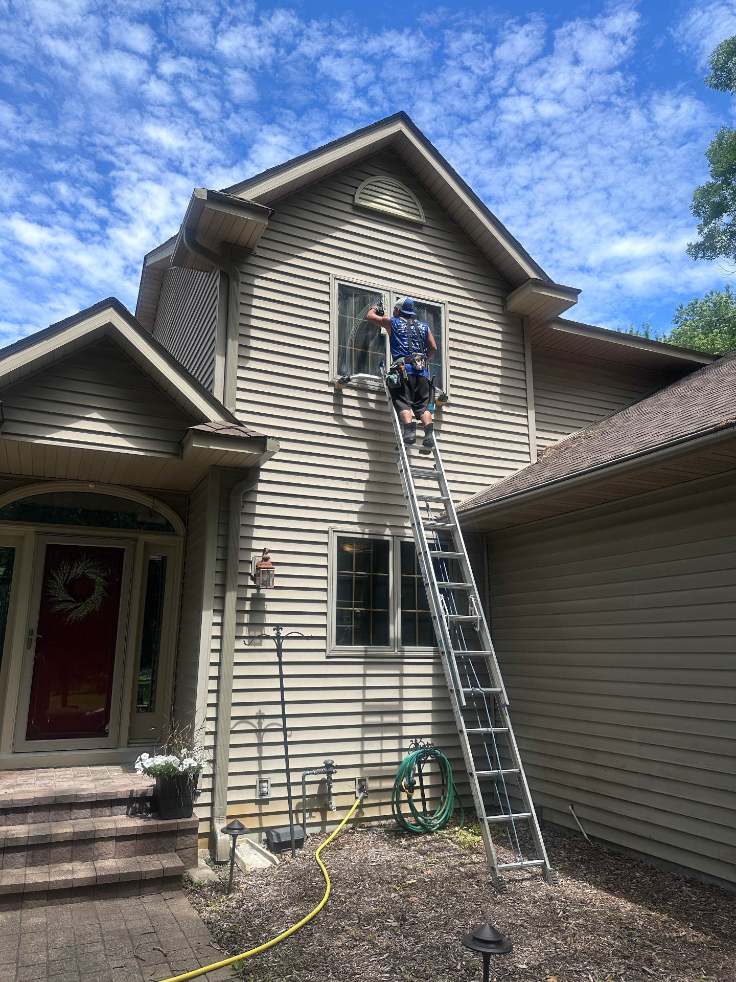 Starbrite technician squeegeeing a second-story window from an extension ladder
